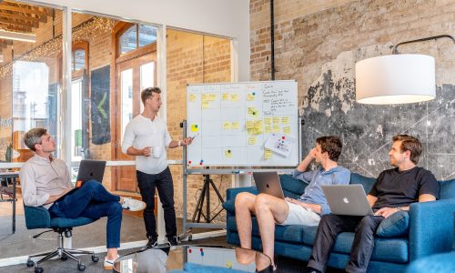 Three men sitting while another man presents in front of a whiteboard