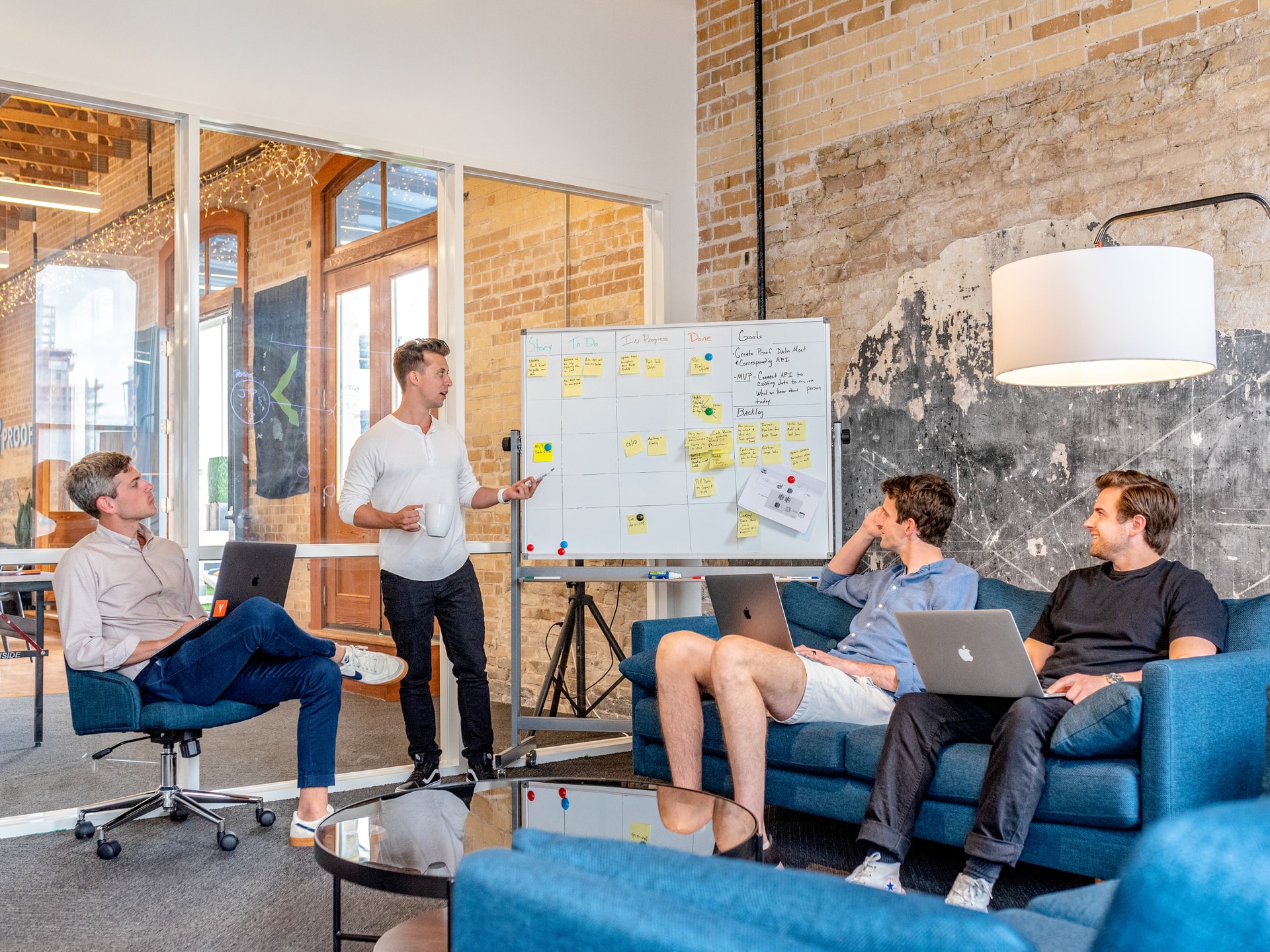 Three men sitting while another man presents in front of a whiteboard