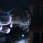 hand holding a magnified lens focusing on a city at nigh time