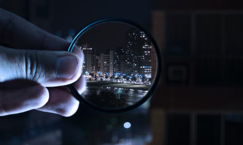 hand holding a magnified lens focusing on a city at nigh time