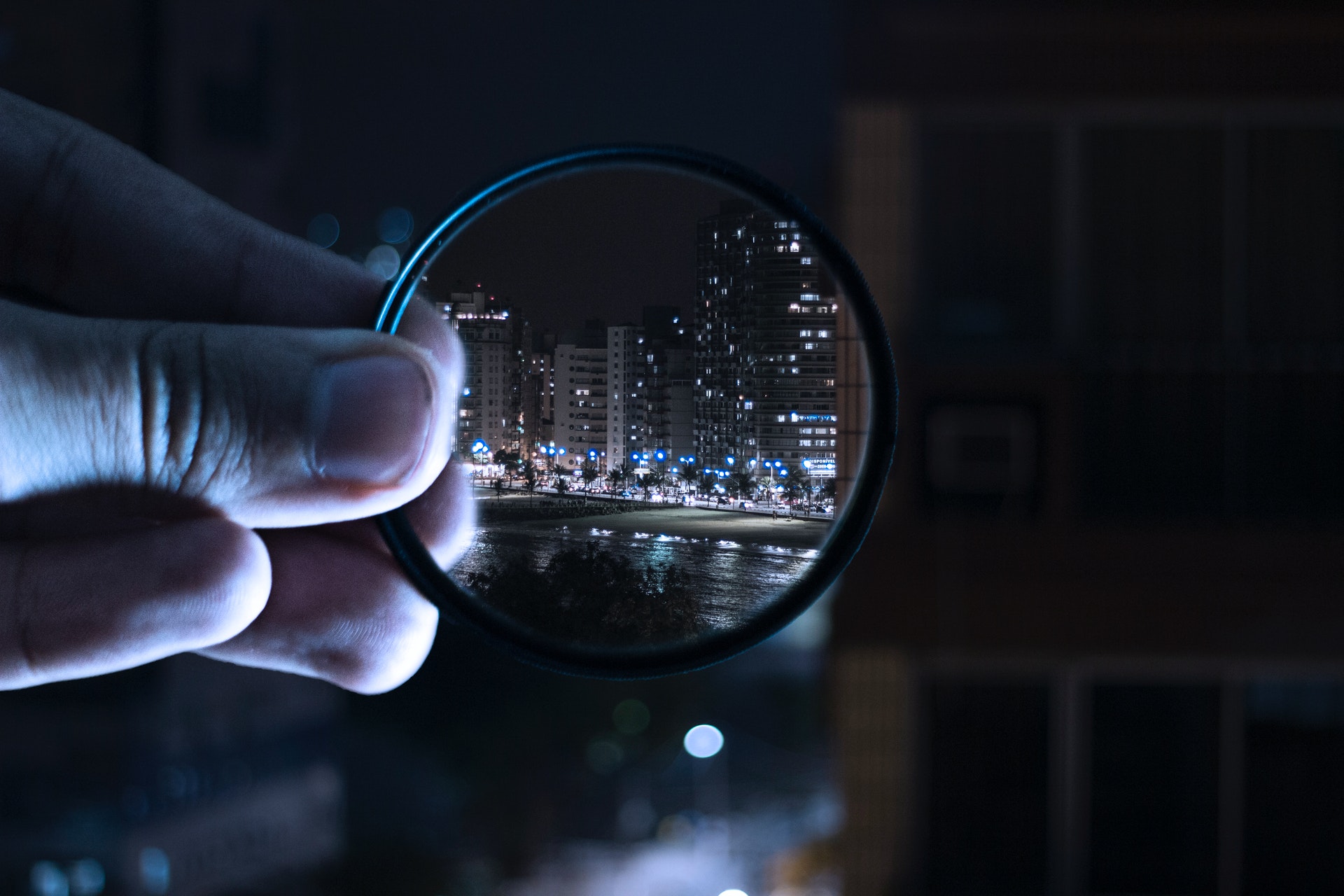 hand holding a magnified lens focusing on a city at nigh time