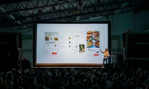 A man presenting to a live audience, both in person and virtually